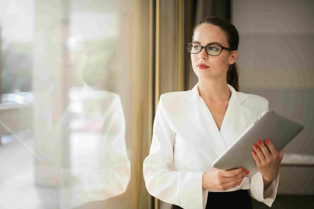 Een zelfverzekerde business consultant kijkt uit het raam van een modern kantoor, ter illustratie van de zoekvraag 'hoe vind ik overheidsopdrachten als zzp'er' middels strategische tips voor interim opdrachten.